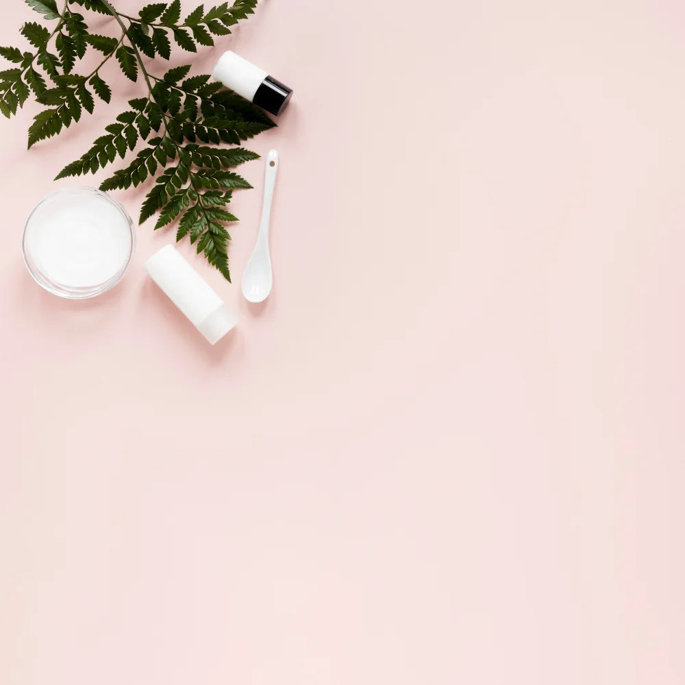 Cosmetic products and a leaf on a light pink background
