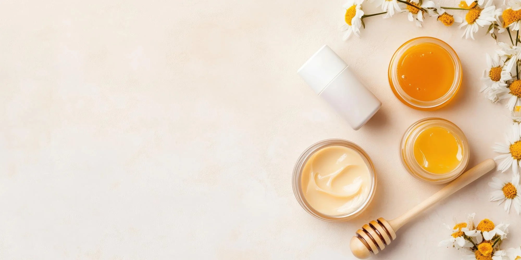 Jars of honey and cream with a wooden honey dipper on a light background
