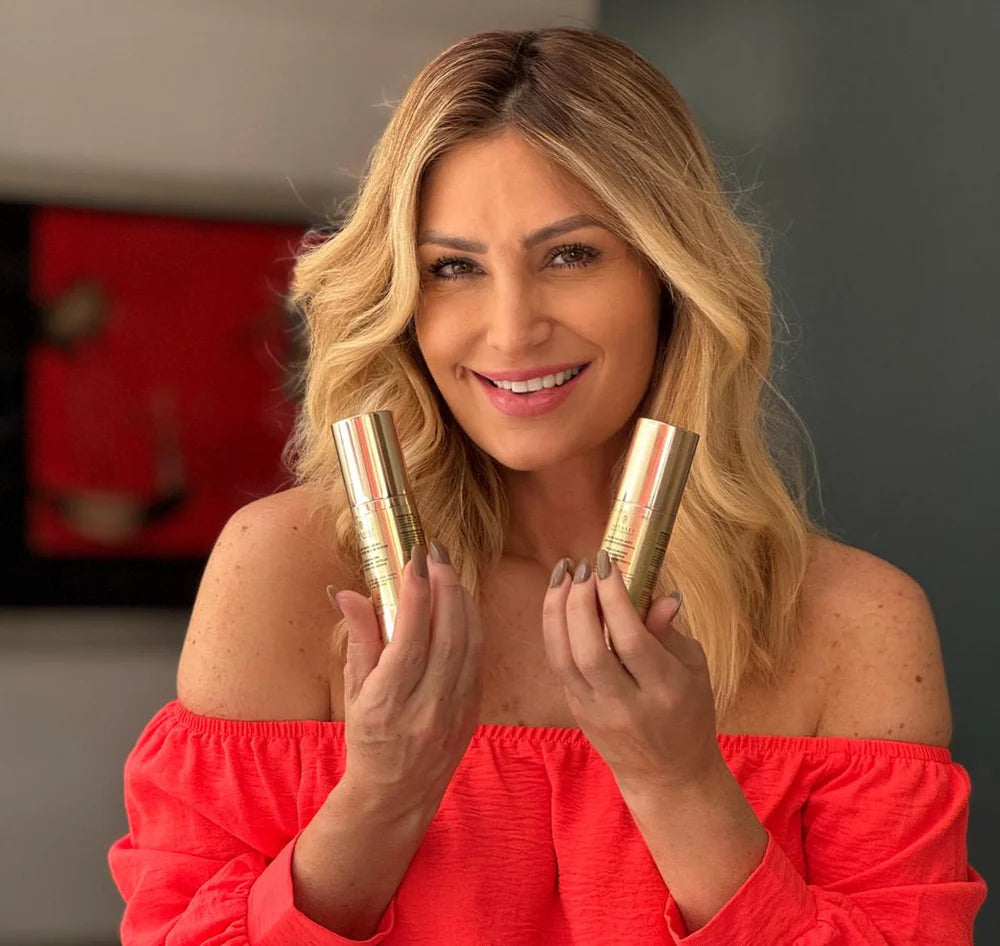 Woman in a red top smiling and holding two BeautyBoost Day Serum bottles.